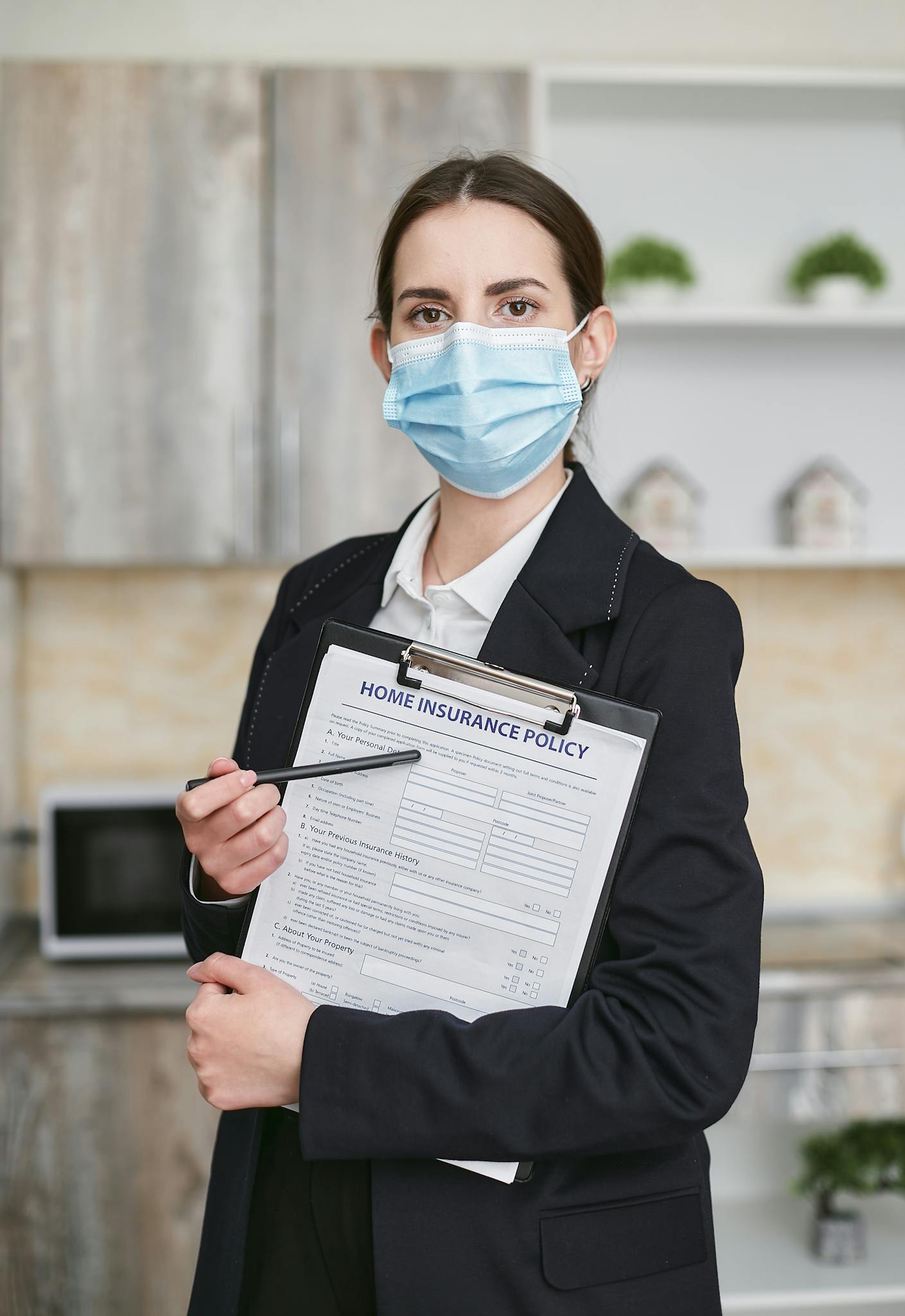 Professional woman with face mask presenting home insurance policy indoors.